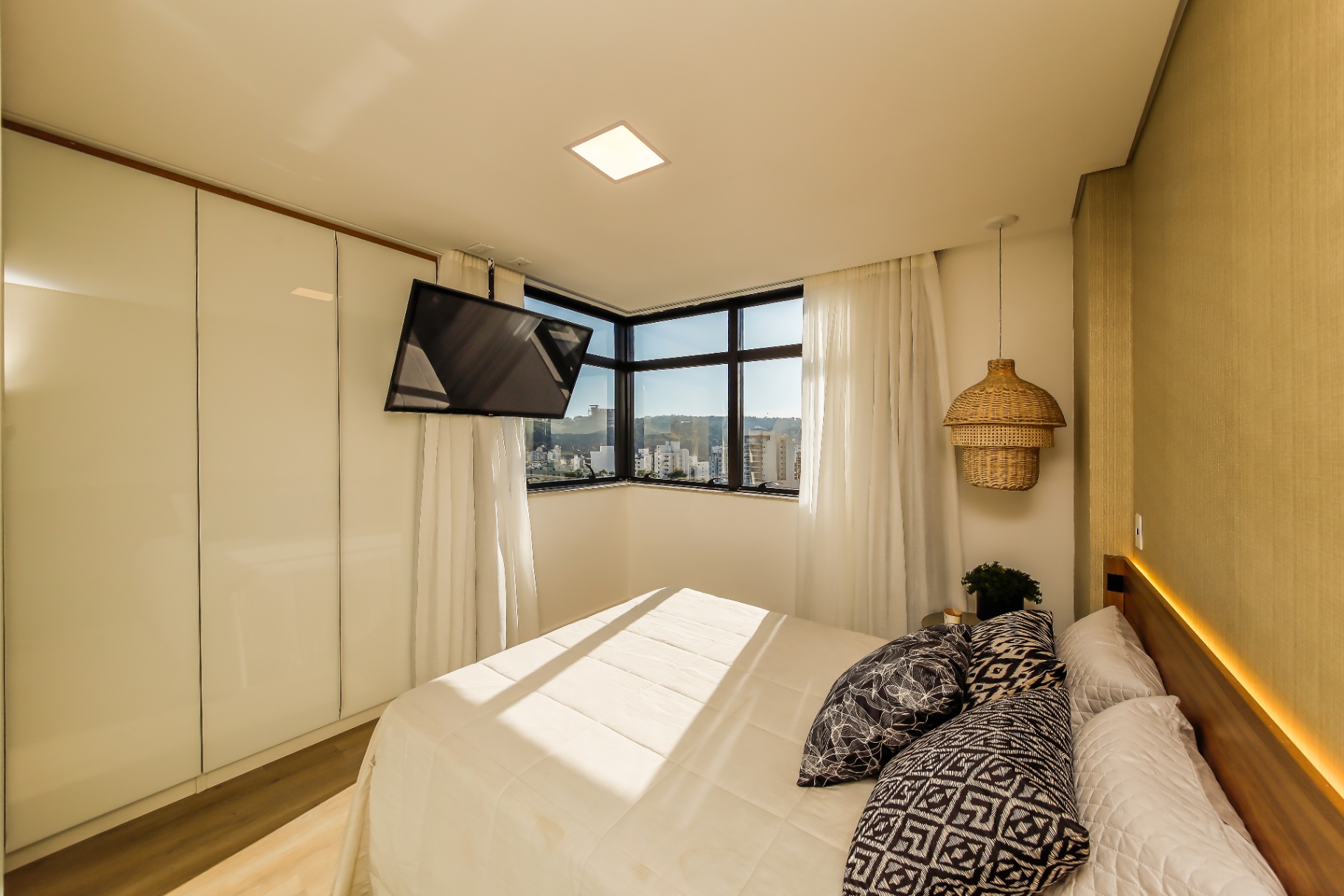 Suíte master decorada com TV, vista panorâmica e cabeceira iluminada