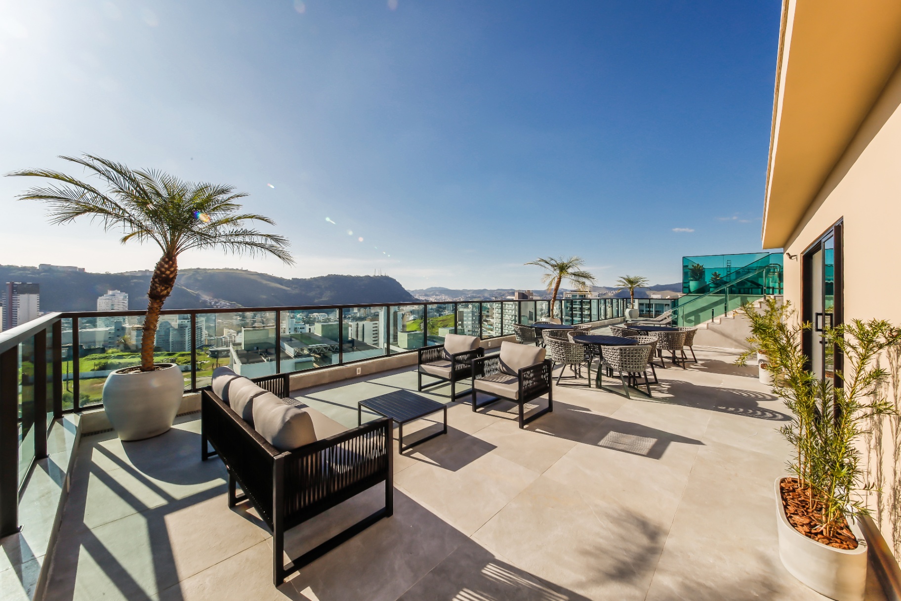 Terraço de convivência com sofás, palmeiras e mesas de jantar ao ar livre